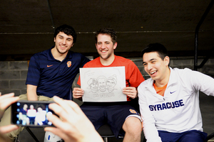 (From left) Kyle Fenton, Jeff Kurkjian and Andy Pregler — the three captains of the Syracuse University mascot team — sit down with an illustration of themselves during halftime during Monday's game.