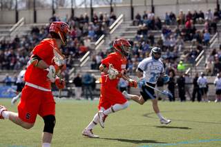 A Syracuse player cradles the ball as he runs up the field. 