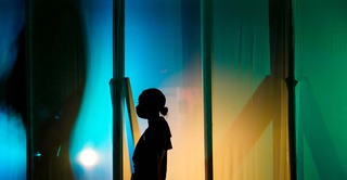 A student stands in shadow waiting to take the stage behind a curtain of colors.  